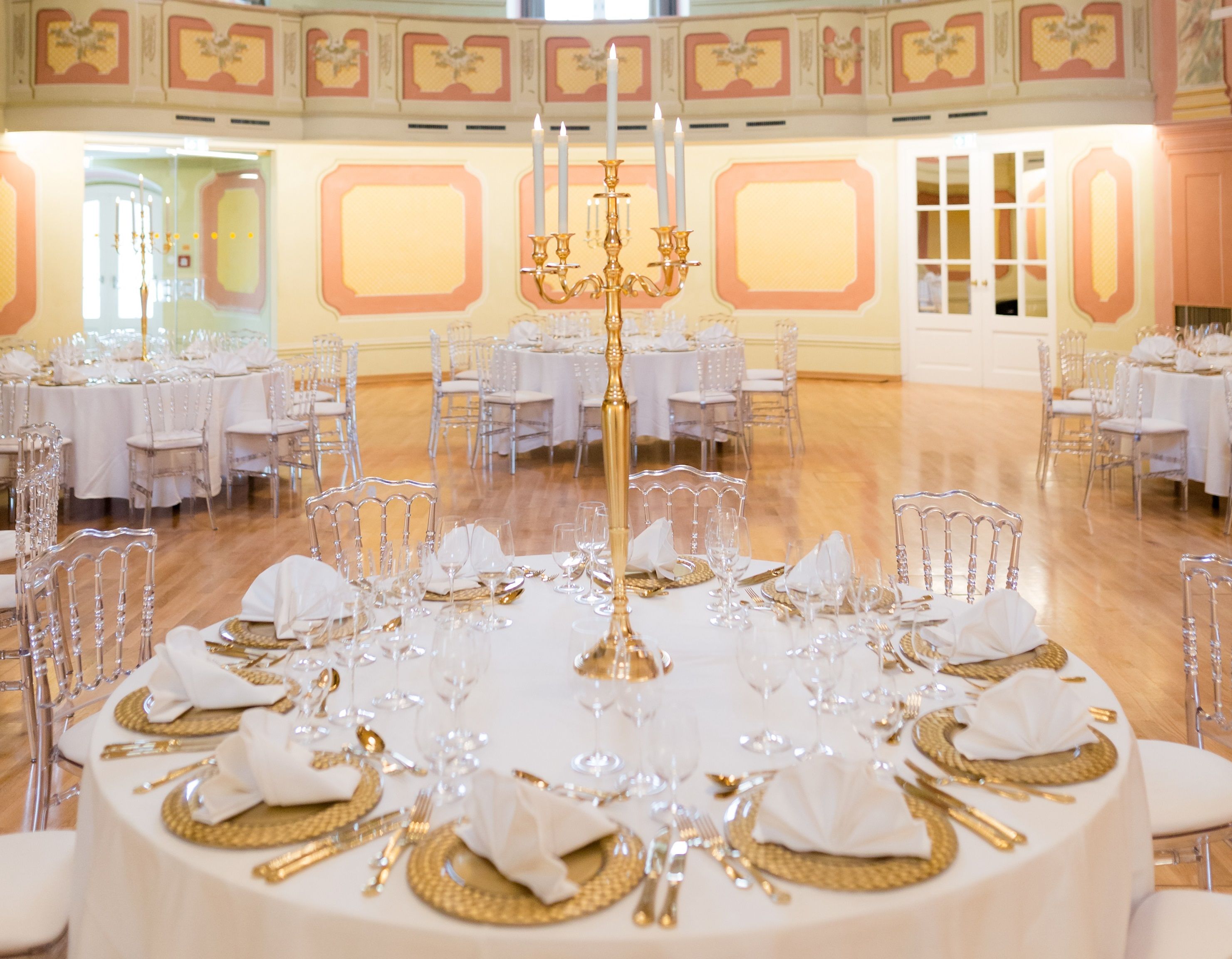 Elegant theater hall with round, festively laid tables and golden candlesticks.