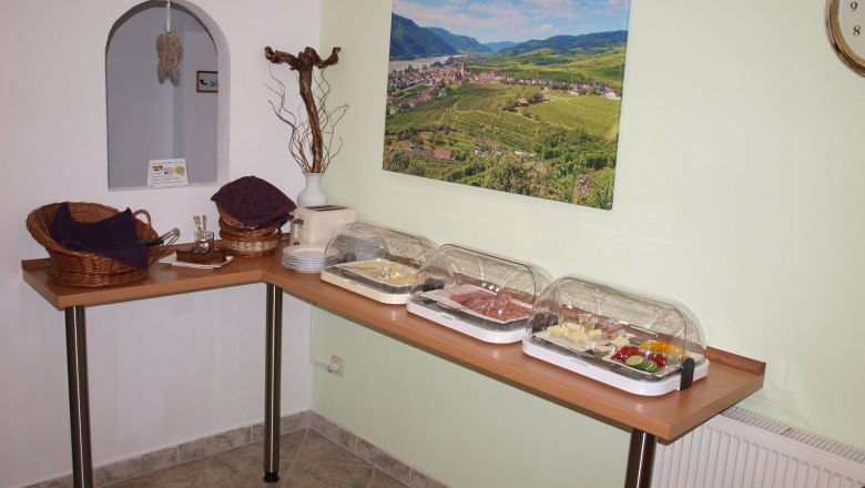Breakfast buffet with cold cuts and vegetables in a room with a landscape picture on the wall.