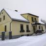 Yellow house in the snow with snow-covered roof and sidewalk.