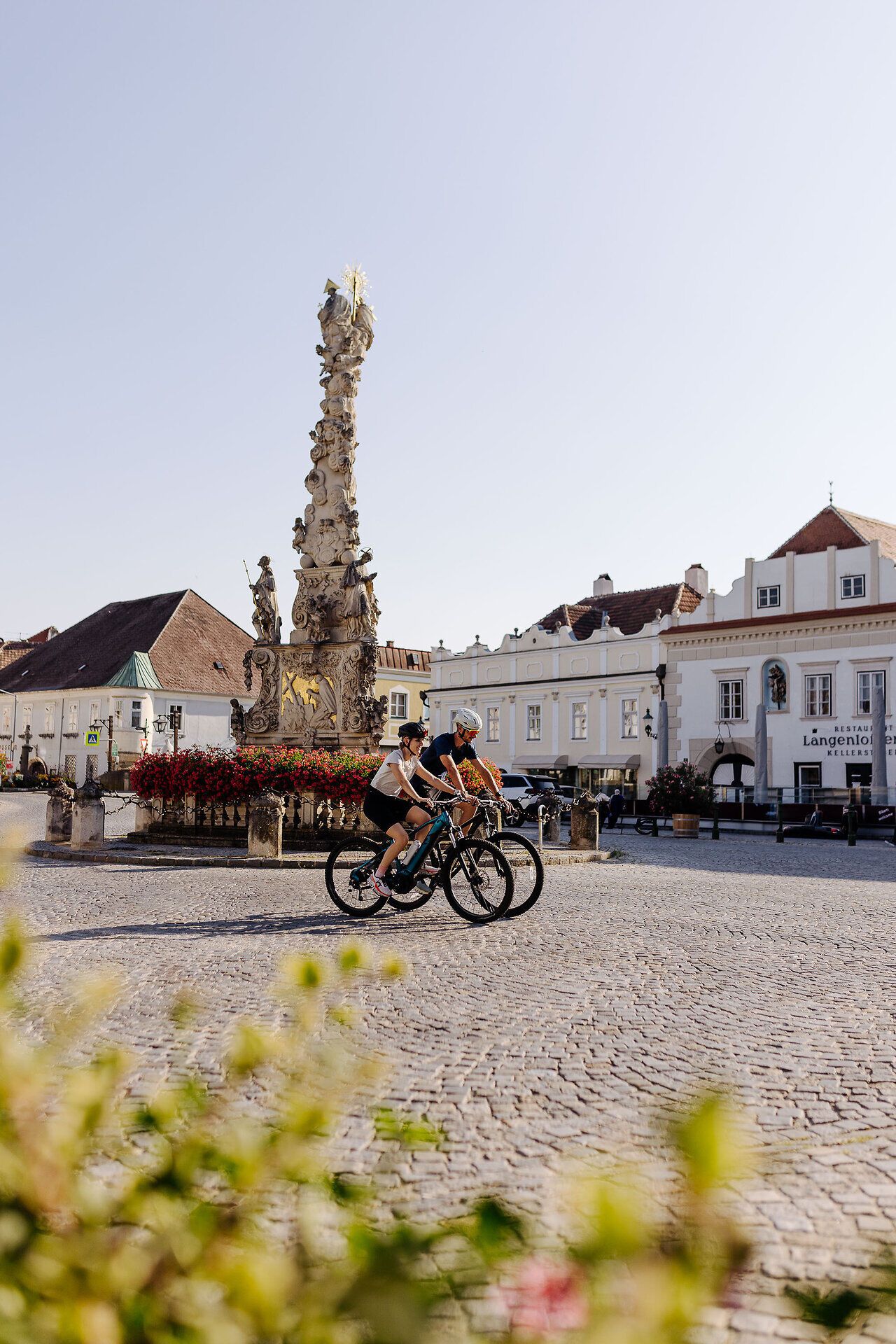Two cyclists on their bikes ride across the main square of Langenlois.
