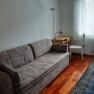 A simply furnished room with a sofa, a desk, a chair and a carpet on a wooden floor.