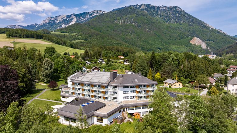 Aerial view of a large hotel in a green, mountainous landscape.