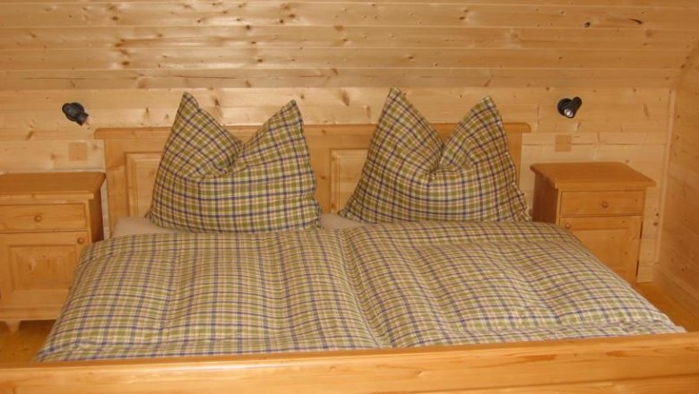 Wooden bedroom with checkered double bed and bedside tables.
