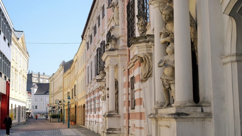 Street with historical buildings and statues in a city.