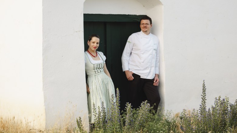 Two people are standing in a doorway in front of a white building.