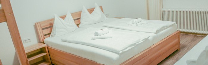 A cozy double bed in a bright room with a wooden frame and white sheets, decorated with folded towels.