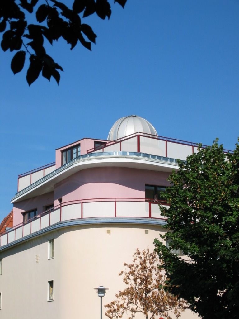 A modern building with a dome on the roof, surrounded by trees, under a clear blue sky.