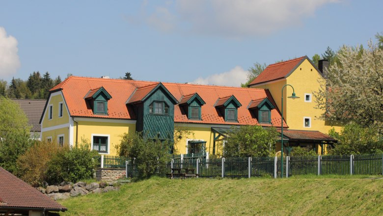 Vacation apartment Zum alten Forsthaus, © Angela Schmid Yellow house with a red roof and green shutters, surrounded by trees and a fence.