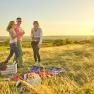 Three people having a picnic in a meadow at sunset.