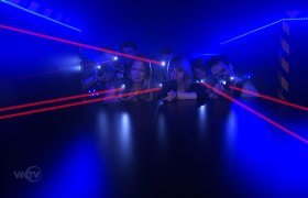 People play laser tag in a dark room with blue lights and red laser beams.