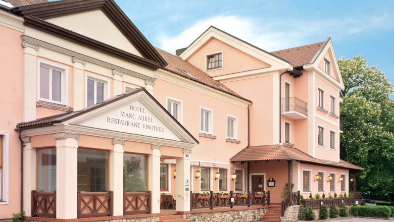Exterior view of the Hotel Marc Aurel in Petronell-Carnuntum with pink façade and classic entrance.