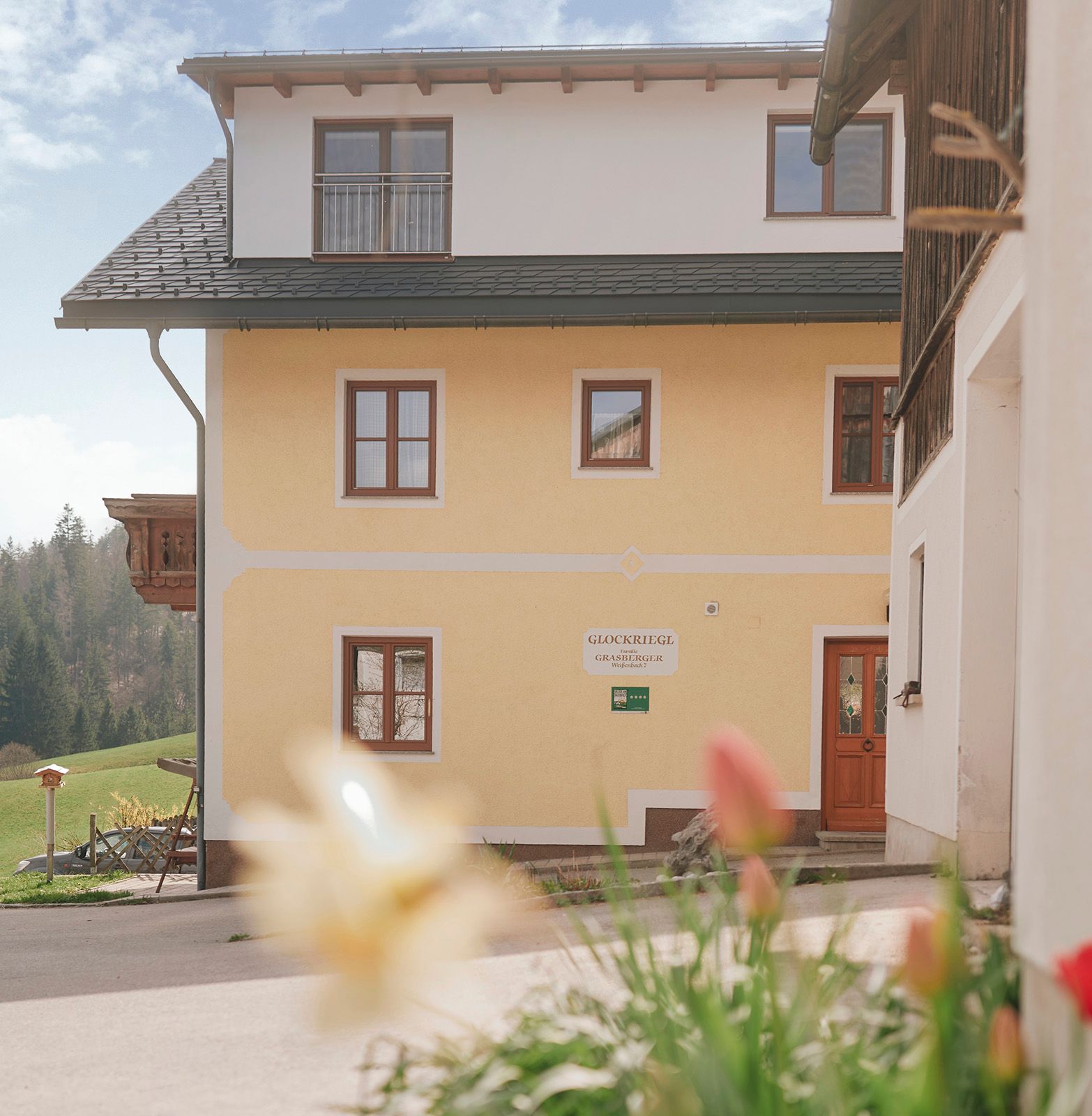 Yellow house with wooden balcony and flowers in the foreground.