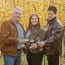 Three people clink glasses in an autumnal vineyard.