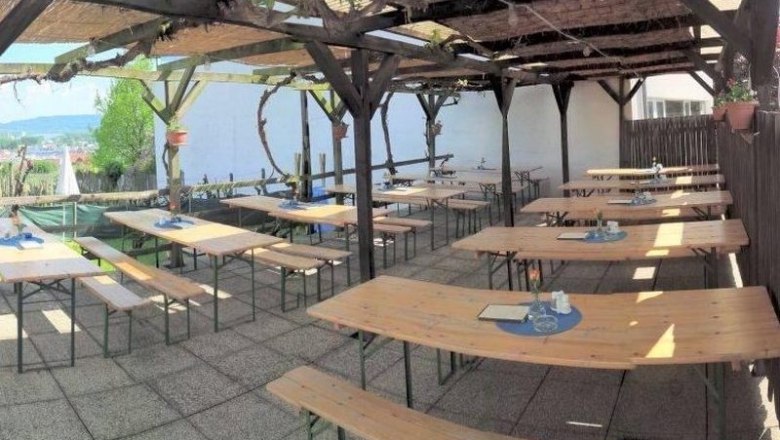 Empty wine tavern terrace with wooden benches and tables under a pergola.