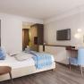 Modern furnished hotel room with double bed, blue chair, wall mirror and flat screen TV.