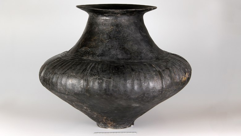 Large, dark conical-necked vessel with decorations on a light background.
