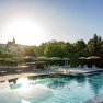 Outdoor area of a hotel with pool, sun loungers and umbrellas, surrounded by trees.