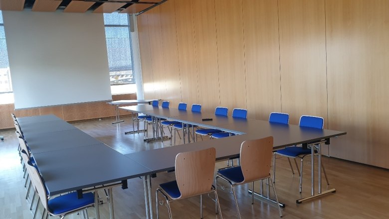 An empty conference room with U-shaped tables and blue chairs.
