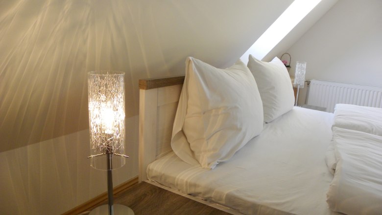 Cozy bedroom with sloping ceiling, bed and bedside lamp.