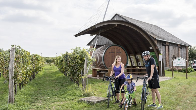 A family with bicycles in front of a winery with a large barrel in Hohenruppersdorf.