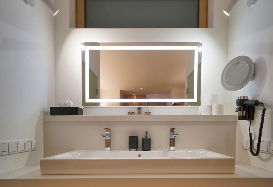 Modern washbasin with illuminated mirror, two taps, soap dispenser and hairdryer.