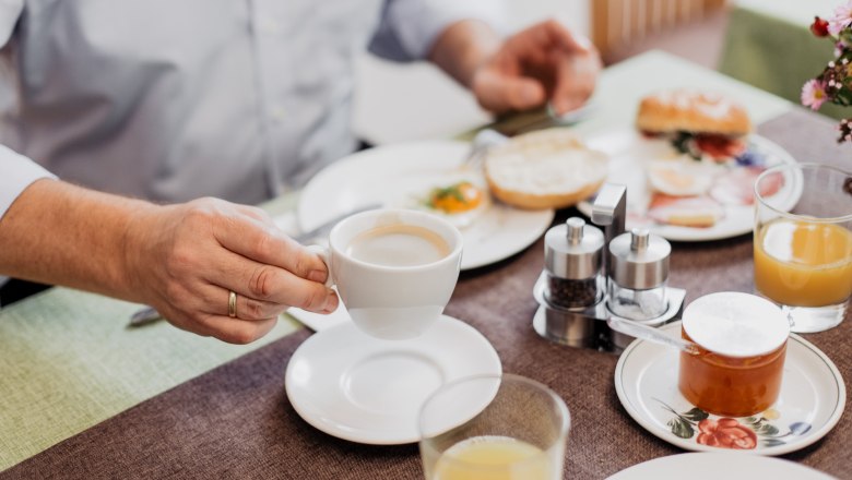 Person holding a cup of coffee over a laid breakfast table.