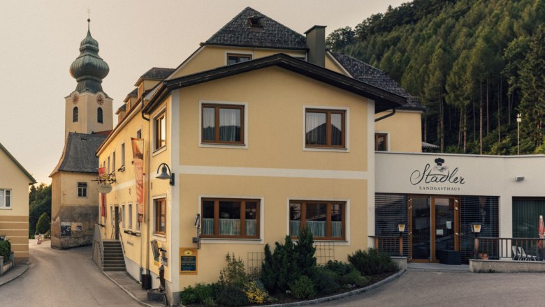 Yellow building with the inscription 'Stadler Landgasthaus' and a church in the background.