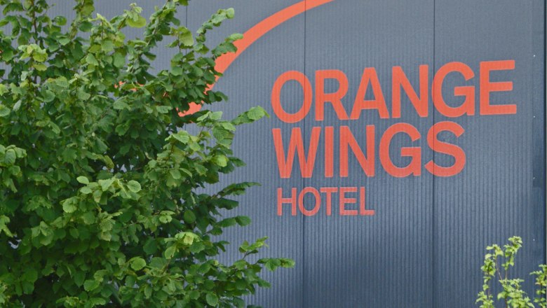 Logo of the Orange Wings Hotel on a wall with plants in the foreground.
