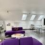 Modern loft with purple sofas, dining table and kitchenette under skylights.