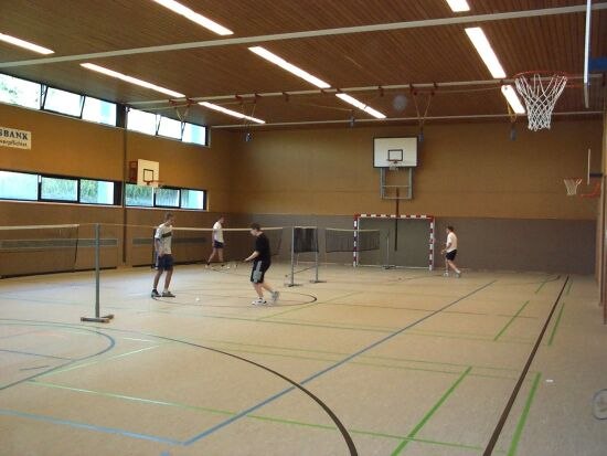 Interior view of a sports hall with badminton players and basketball hoop.