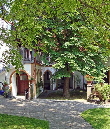 An idyllic courtyard with a large tree, surrounded by a building with arcades and balconies.