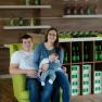 A couple with a baby sits on a green armchair in a winery.