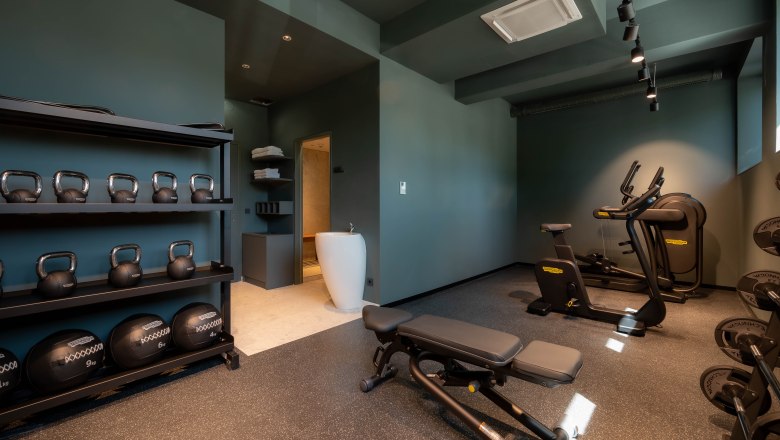 Modern fitness room with kettlebells, dumbbells, treadmill and ergometer.