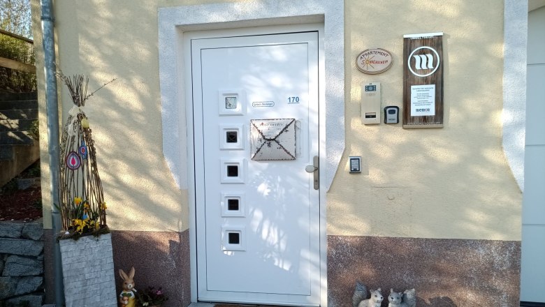 A warm welcome!, © S. Gritsch-Stockinger Entrance area of a house with decorative elements such as a rabbit, a welcome sign and flowers.