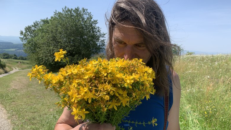 A person smells a bunch of yellow flowers on a country lane.