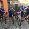 Four cyclists in blue jerseys with New Zealand flags in front of a building.