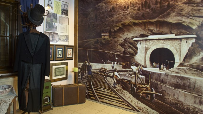 Interior view of the Ghega Museum with a historical suit, pictures and a large mural of a railroad tunnel.