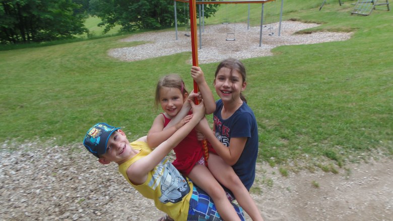 Three children swinging happily on a ropeway in a playground.