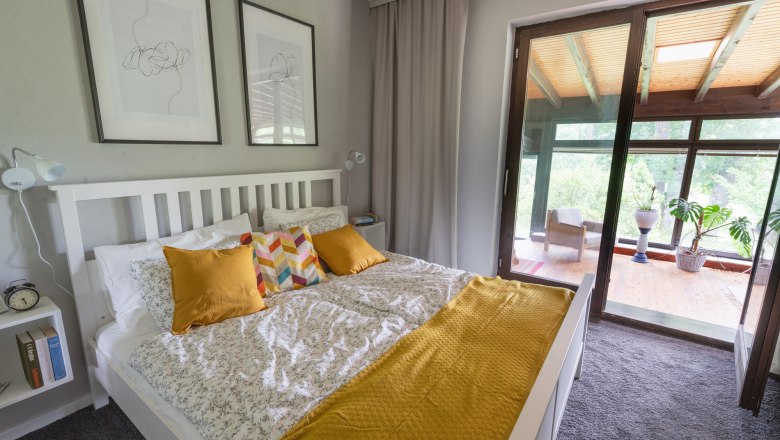A cozy bedroom with a white bed, yellow cushions and a terrace with plants in the background.