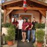 Five people stand in front of the entrance to an inn with a wooden veranda and plants.