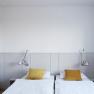 Modern guest room with two single beds, yellow cushions and wall lamps.