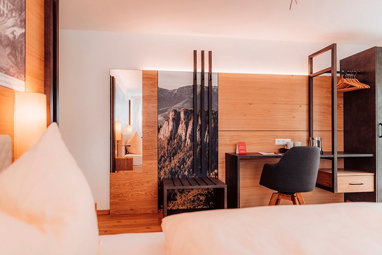 Modern hotel room with wood paneling, desk and chair.
