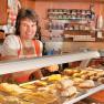 Woman in traditional dress behind a counter with pastries in a pastry shop.