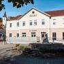 A building with the inscription 'B&auml;renhof' and 'bed - breakfast' in a sunny setting with a fountain in the foreground.