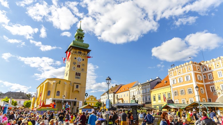 Crowd on a busy square in Retz with a striking clock tower in the background.