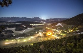 Nocturnal landscape view of Prigglitz with illuminated houses and mountains in the background.