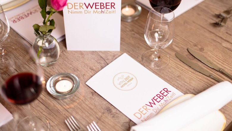 Table setting at Restaurant Der Weber with menu cards, wine glasses and a rose.