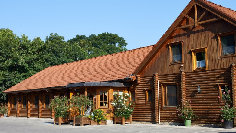 Log cabin with red tiled roof and plants in front of it.