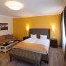 Hotel room with double bed, yellow wall, sofa, table and curtains.