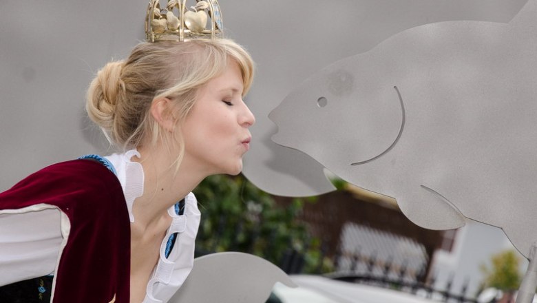 Woman with crown kisses carp sculpture.